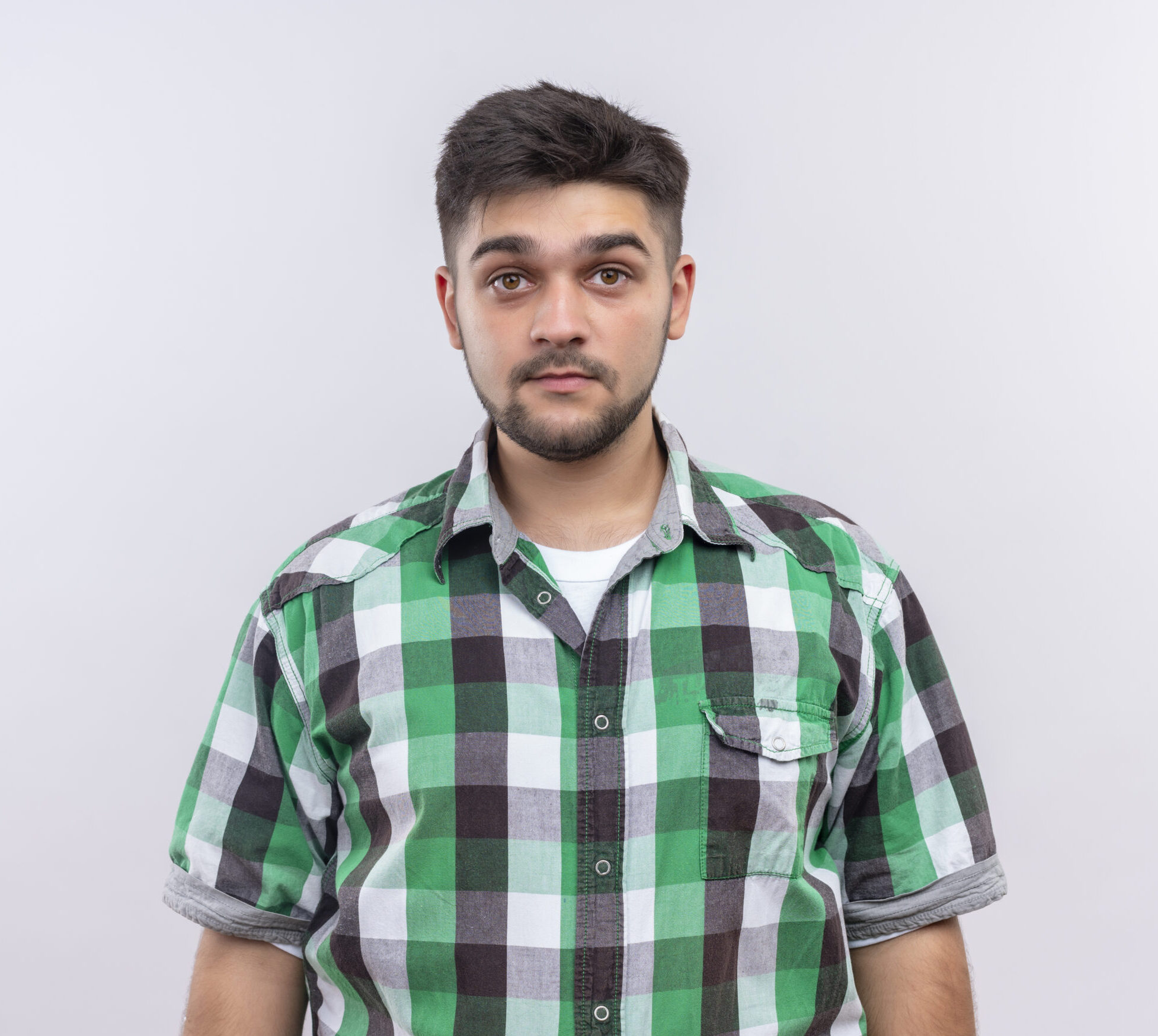 young handsome guy wearing checkered shirt looking at camera standing emotionless over white background